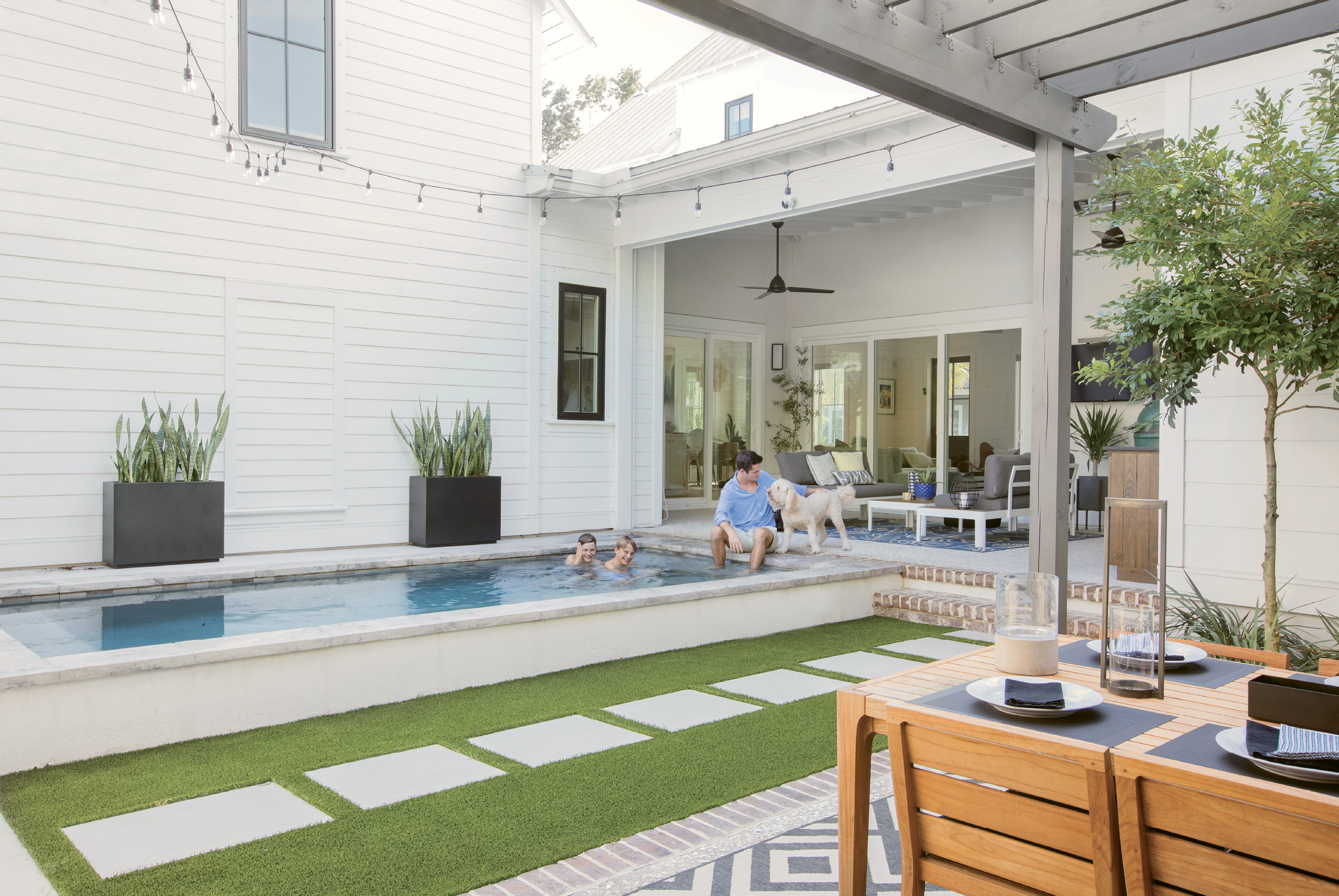 Fun Zone: Three sliding glass doorways open to the outdoor entertaining areas, including a lounge space with aluminum and teak love seats from AllModern and a woven lantern from Lyndon Leigh, Cristian’s “kitchen,” a compact pool where the boys and goldendoodle Kylie splash and play, and the pergola-covered dining area with a teak table and chairs.