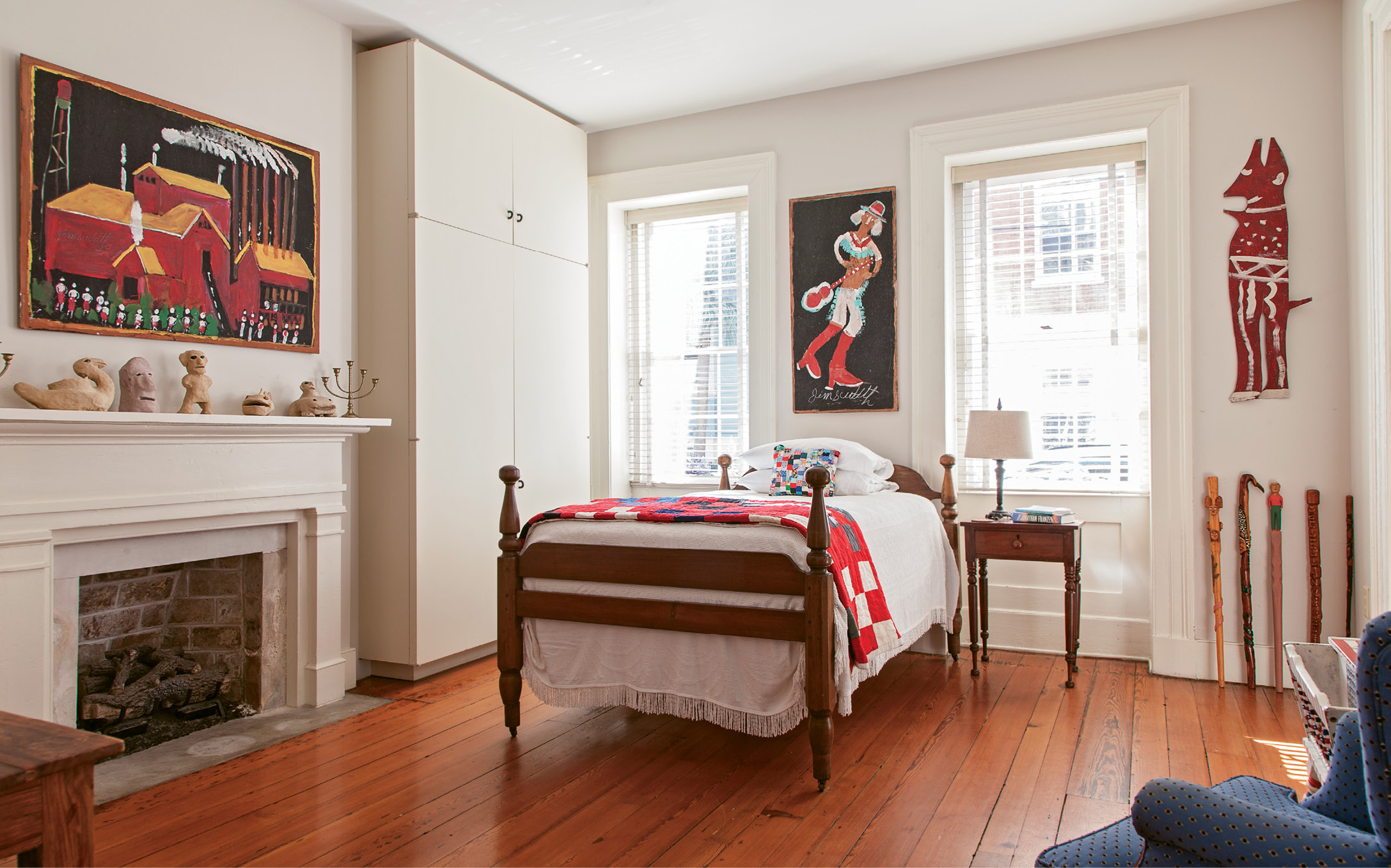 A guest room plays host to several paintings by Jimmy Lee Sudduth, of Alabama, including Sawmill above the fireplace and Musician above the bed.